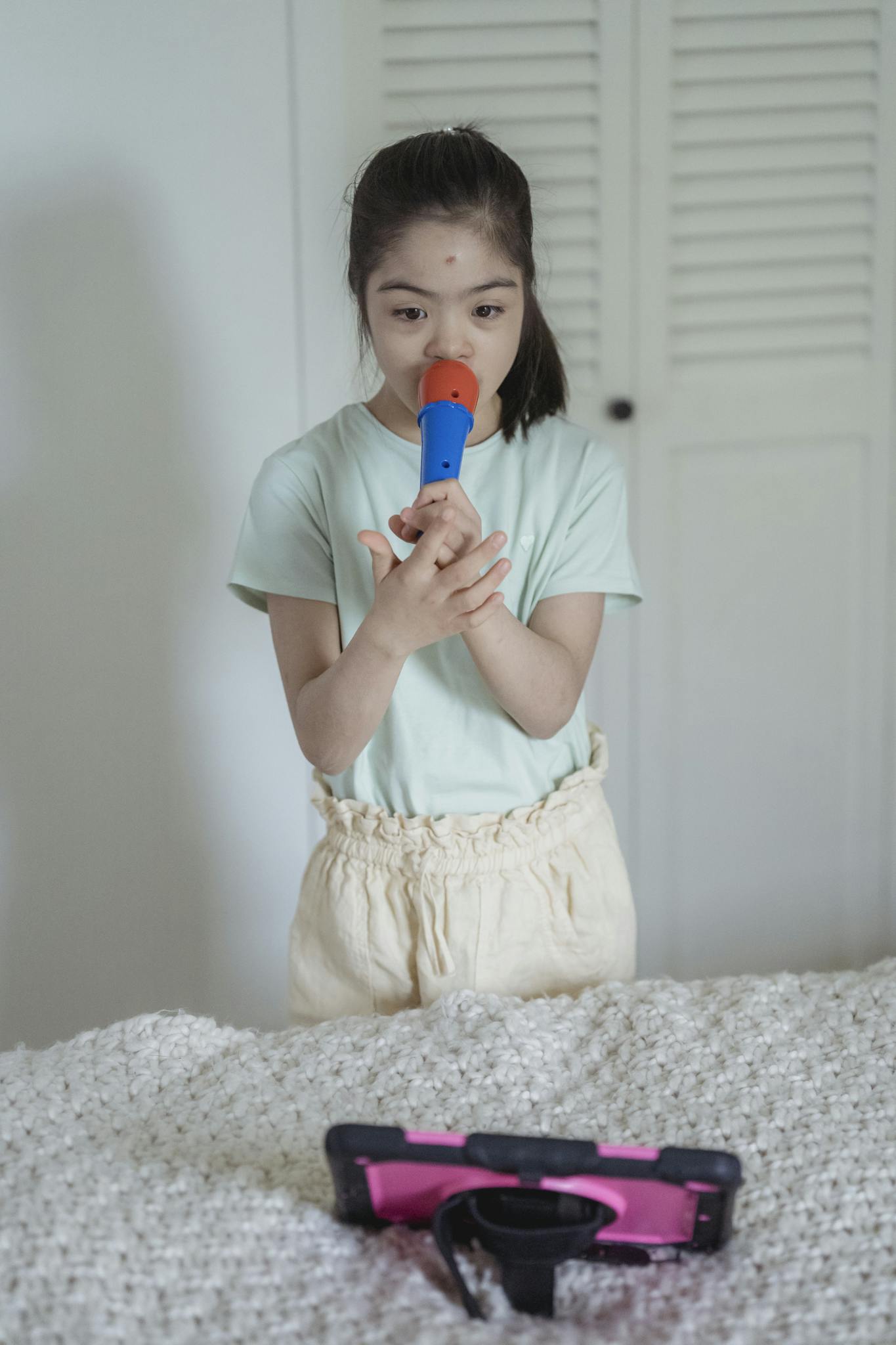 Child singing with a toy microphone indoors, engaging with a digital tablet.