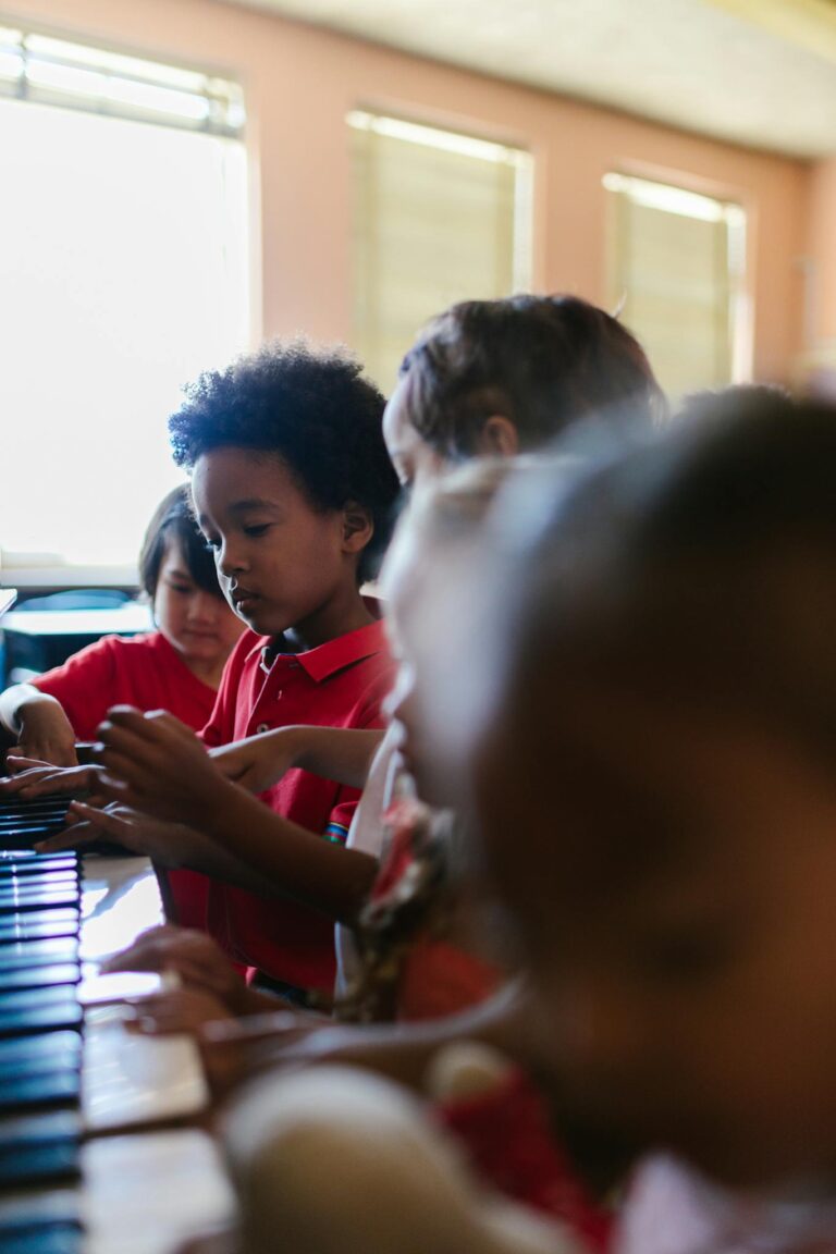 Group of children in a bright classroom learning to play piano together.
