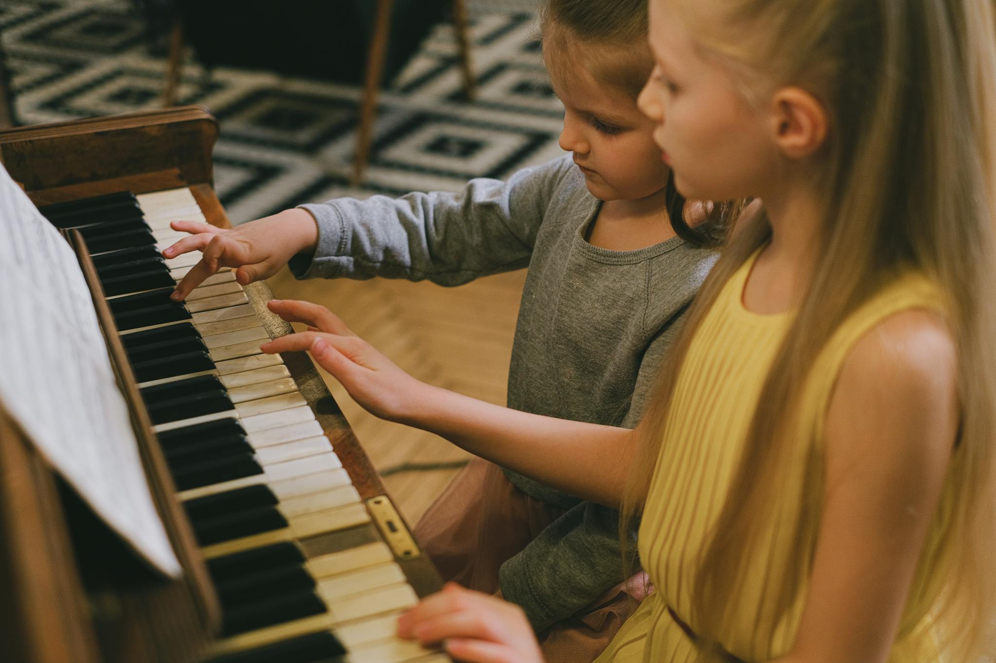 Two young girls playing piano together, sharing a musical moment indoors.